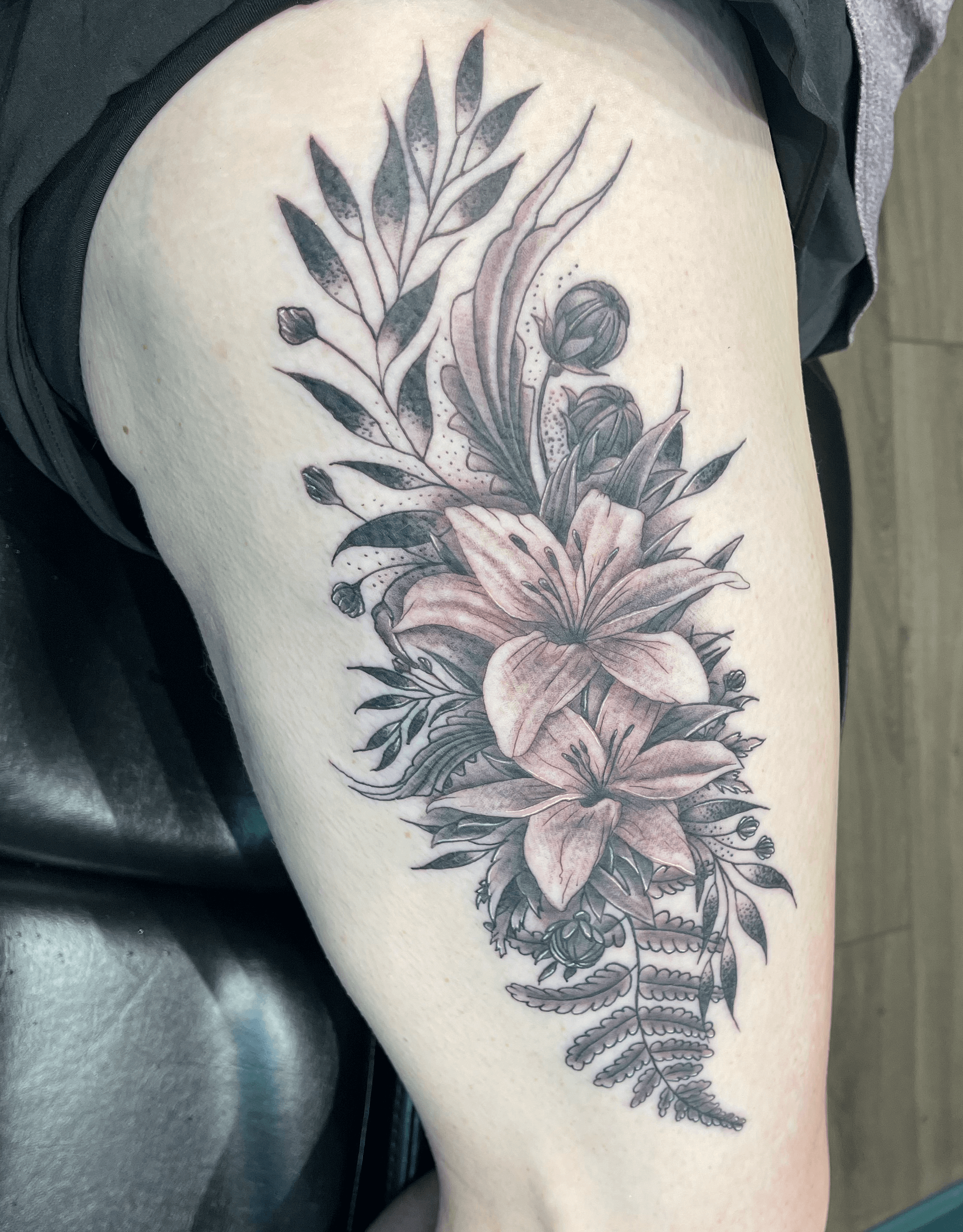 Floral tattoo with two lilies in the centre in black and grey on the thigh